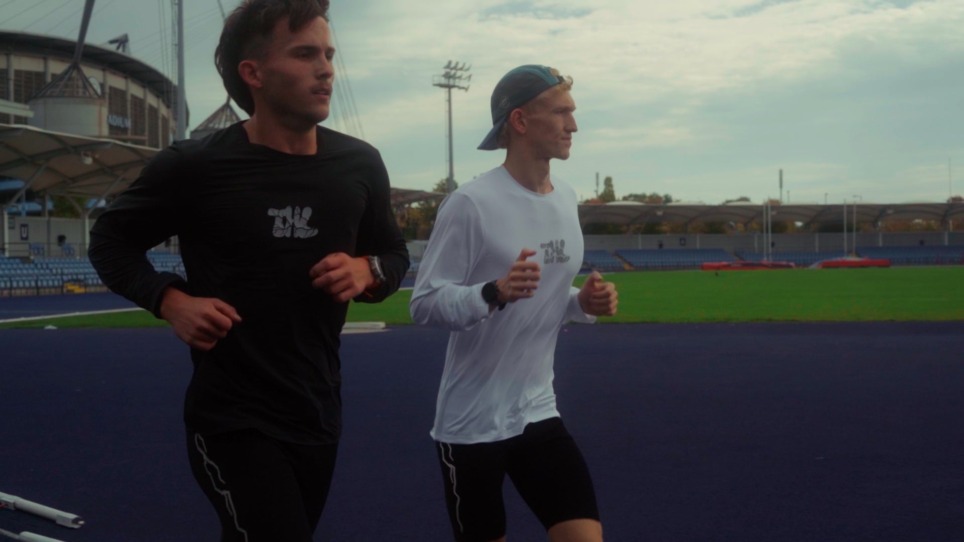 Two runners on a track with stadium in the background