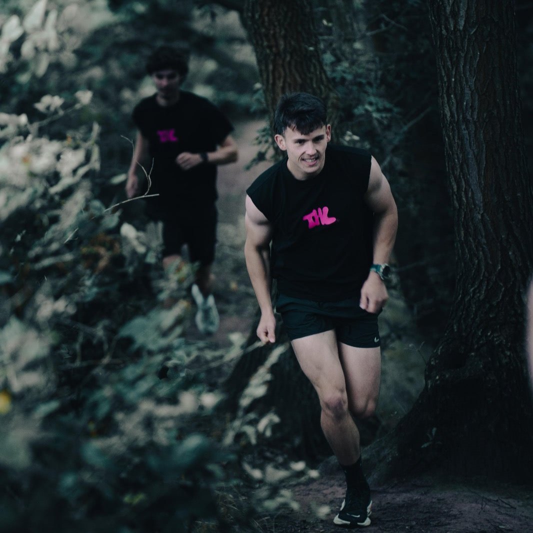 2 Runners running through a forest wearing The Hybrid Life T Shirt and Tank top